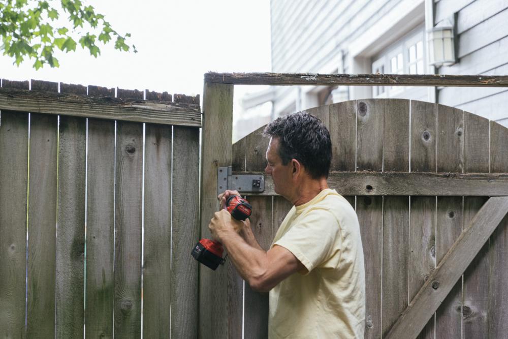 Using a drill to remove the fence gate hinges from the main fence.