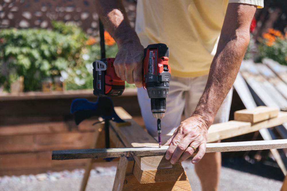 Using a drill to reattach the old fence boards to the new Z-frame.