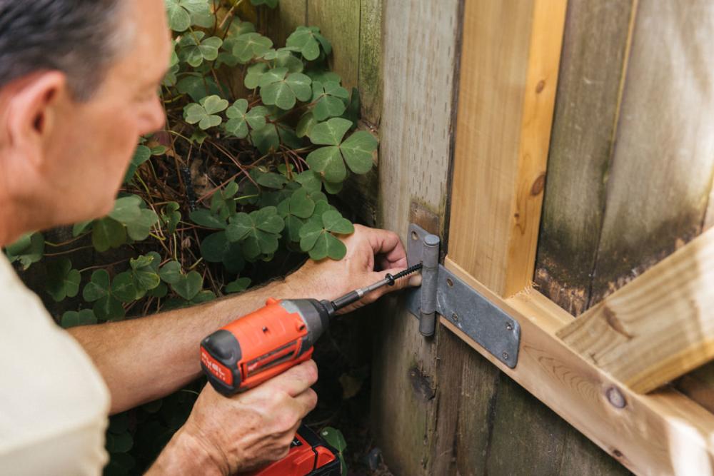 Using a drill to install the hinges on the fence.