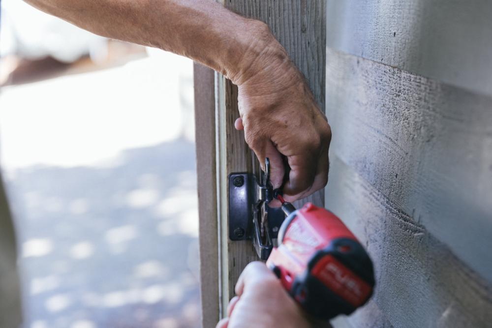 Using a drill to re-attach the latch on the fence. 