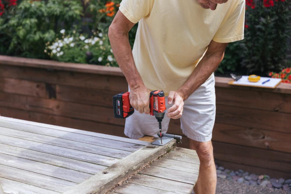 Using a drill to remove the hinges from the fence gate.