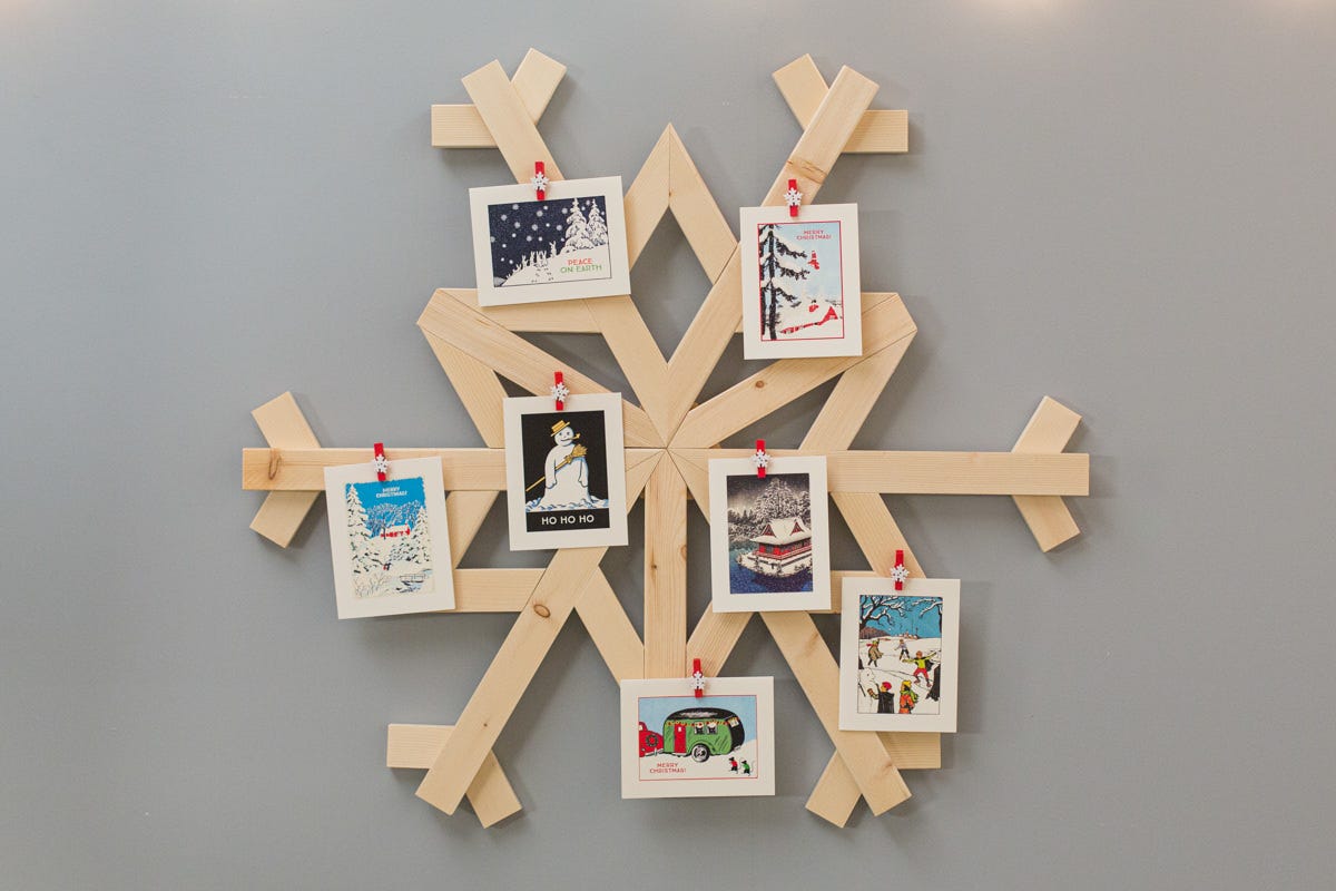 DIY wooden snowflake-shaped Christmas card holder attached to wall, with various Christmas cards pinned to it.