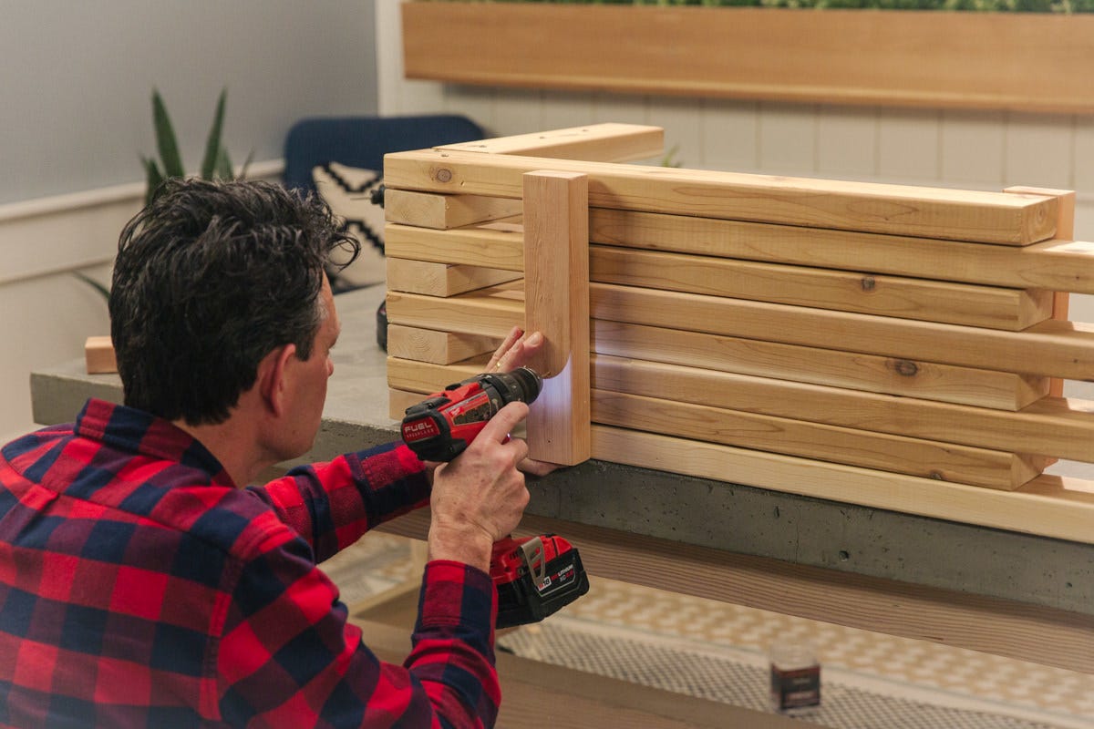 screw bench braces Pre-drilling hole in top brace board laid against wood DIY expandable bench assembly.